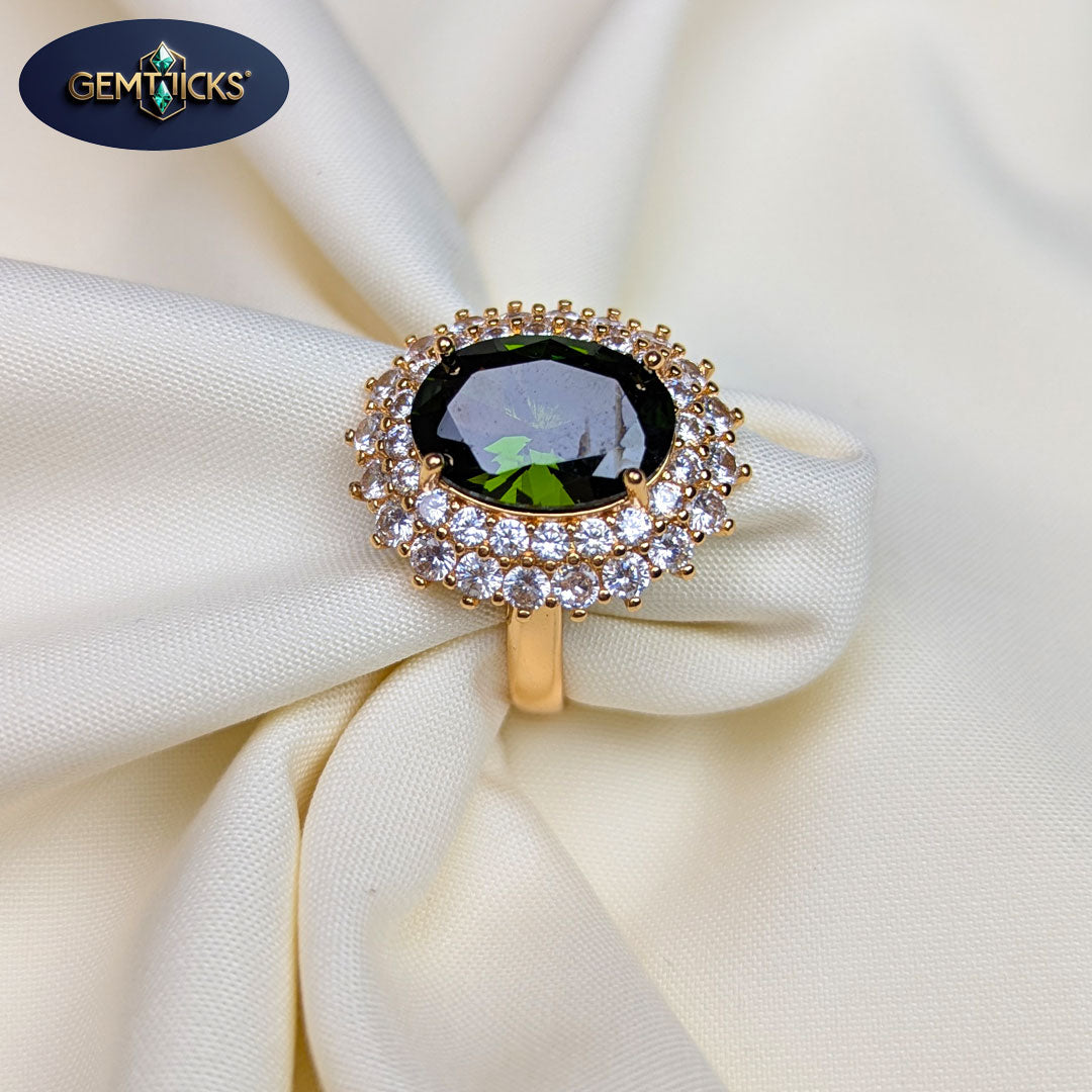 Ring with green gemstone and diamond accents on white fabric, featuring Gemticks logo.